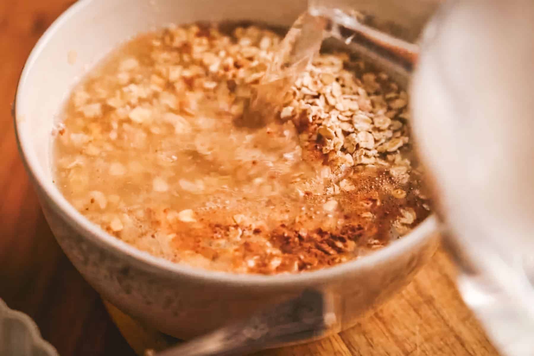Pouring water over a bowl of cinnamon oatmeal with apple.