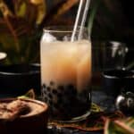 Jasmine milk tea in a clear glass cup sitting on top of a tropical leaf.