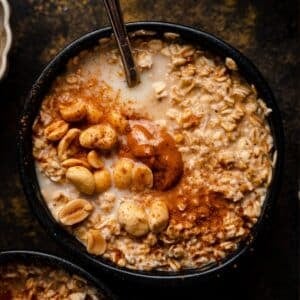 Close up of peanut butter old-fashioned oatmeal in a black bowl with a spoon sticking out of it.