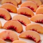Sliced peaches arranged on a parchment paper-lined baking sheet.