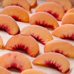 Sliced peaches arranged on a parchment paper-lined baking sheet.