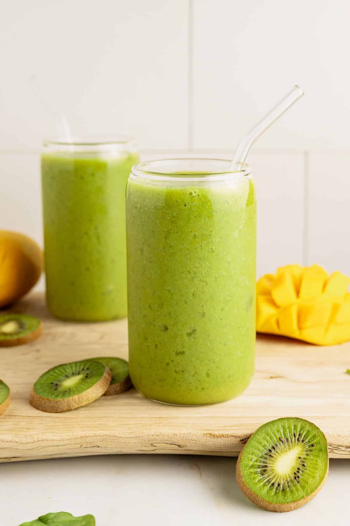 Kiwi smoothie in glasses on top of wooden board.