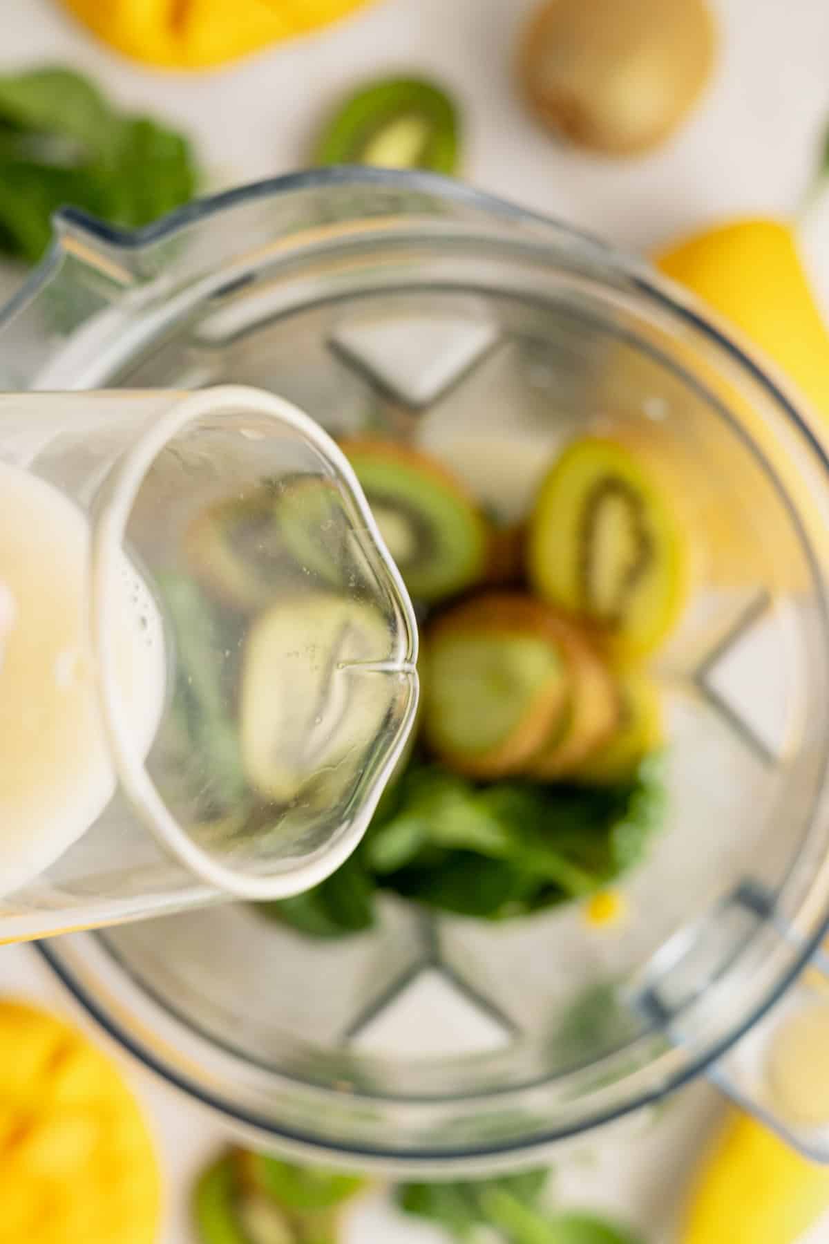 Milk being poured into mango kiwi smoothie.