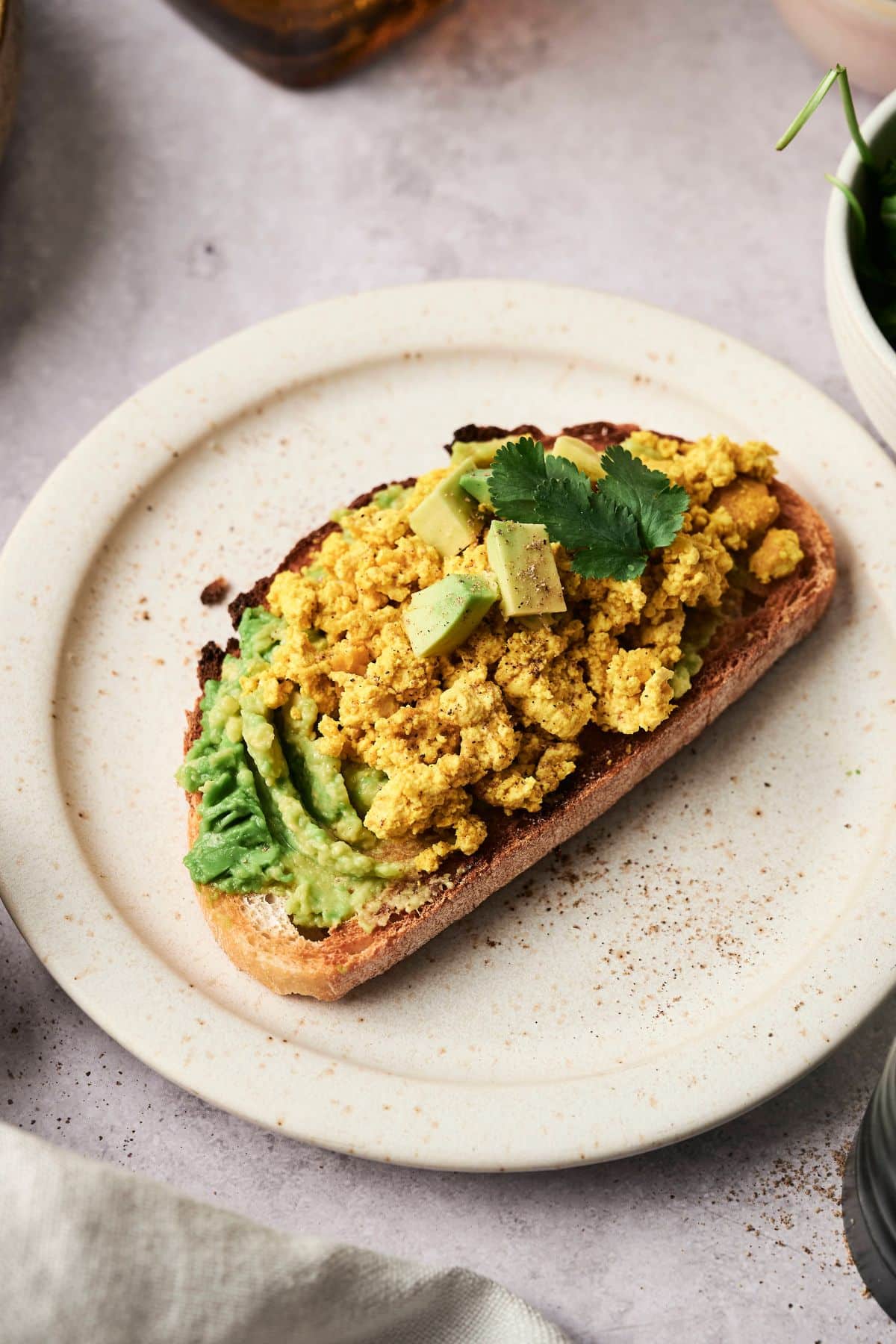 A white place with a piece of toast on top and avocado and vegan scrambled eggs.