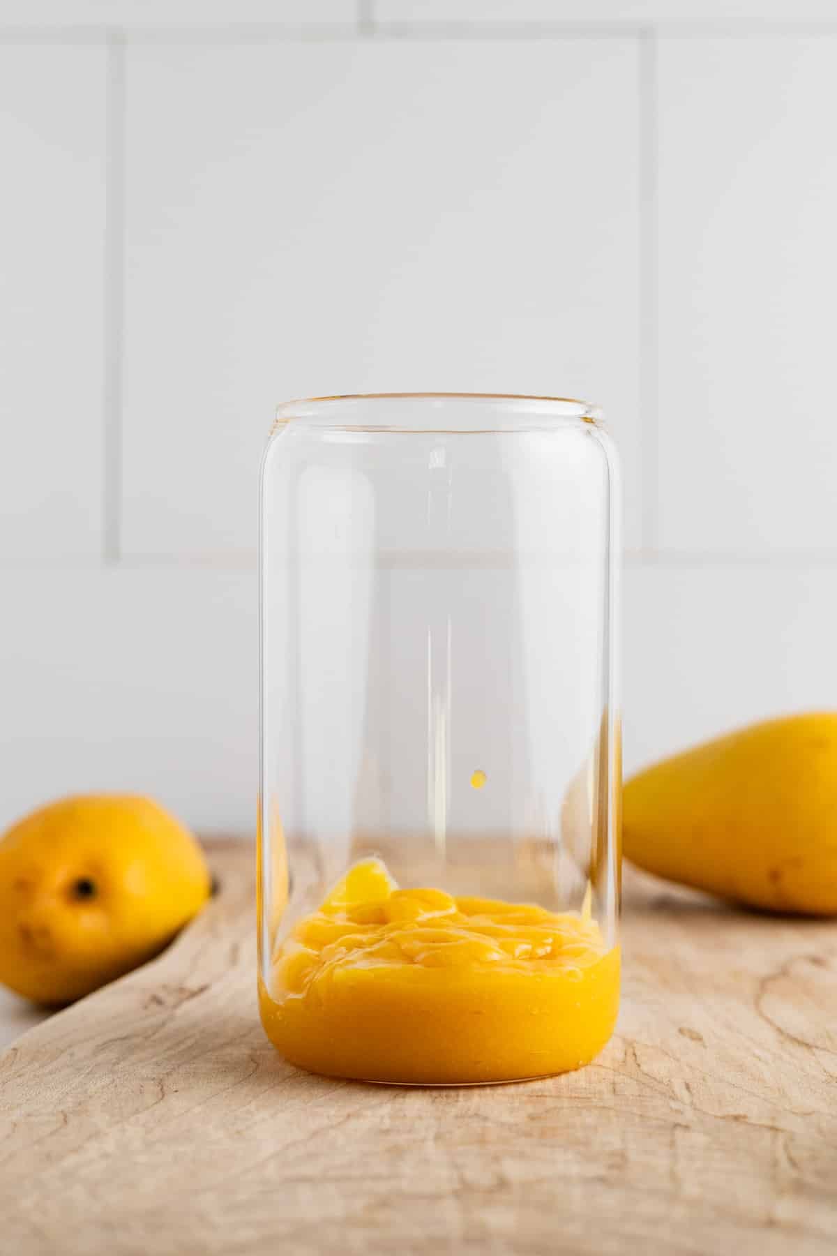Mango puree being added to a clear glass cup.