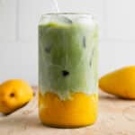 Mango matcha latte in a clear glass cup with fresh mangoes next to it.