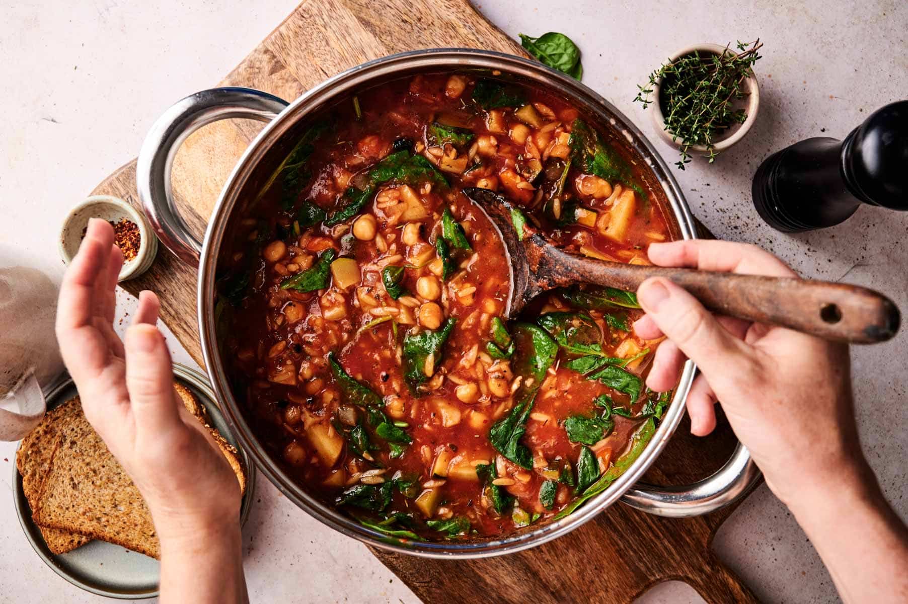 Woman stirring a pot of vegetable noodle soup.