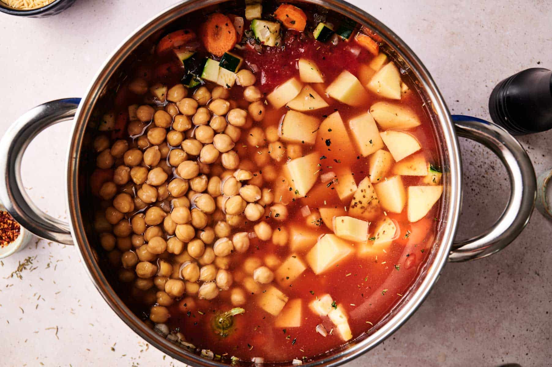 Vegetables, tomato sauce, chickpeas added to stainless steel cooking pot.