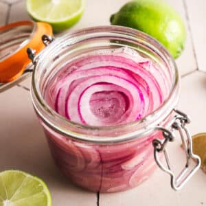 Homemade lime picked onions in a clear glass jar with a glass lid and metal clasp.