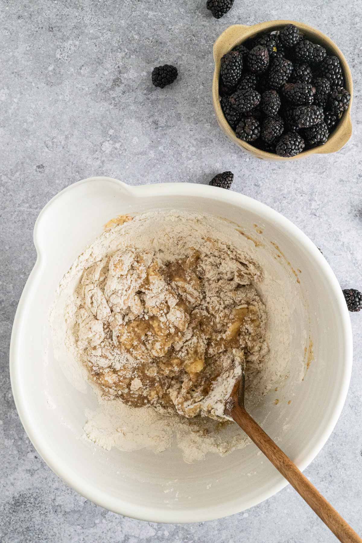 Mixing wet ingredients and dry ingredients for banana blackberry muffins together.