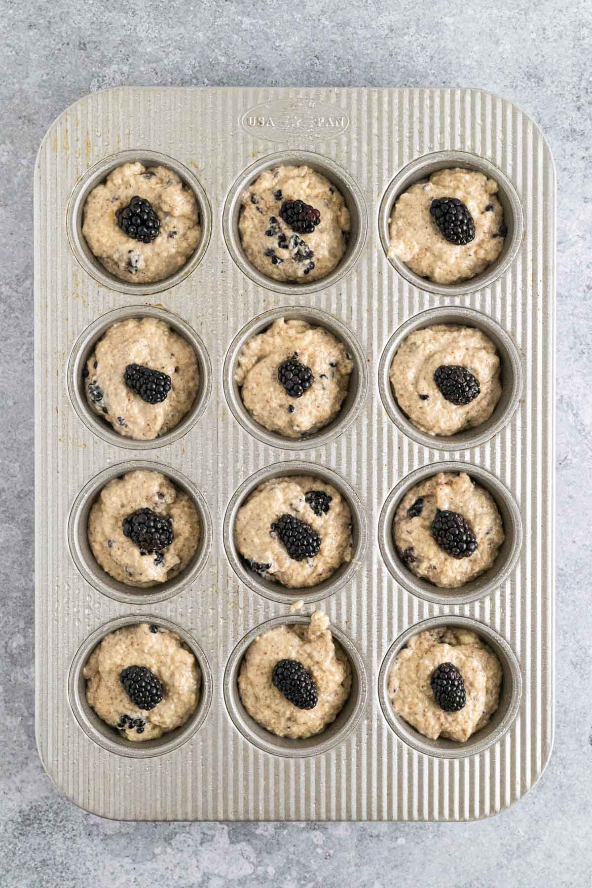 Blackberries on top of muffin batter in muffin tin.