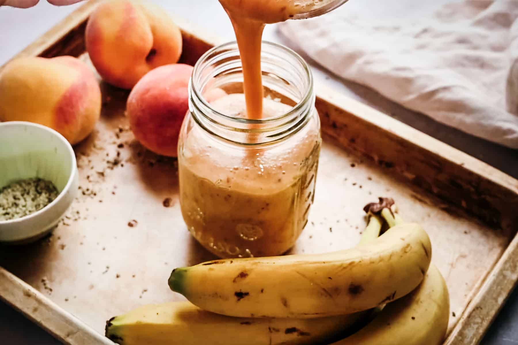 Pouring a homemade peach smoothie into a jar.