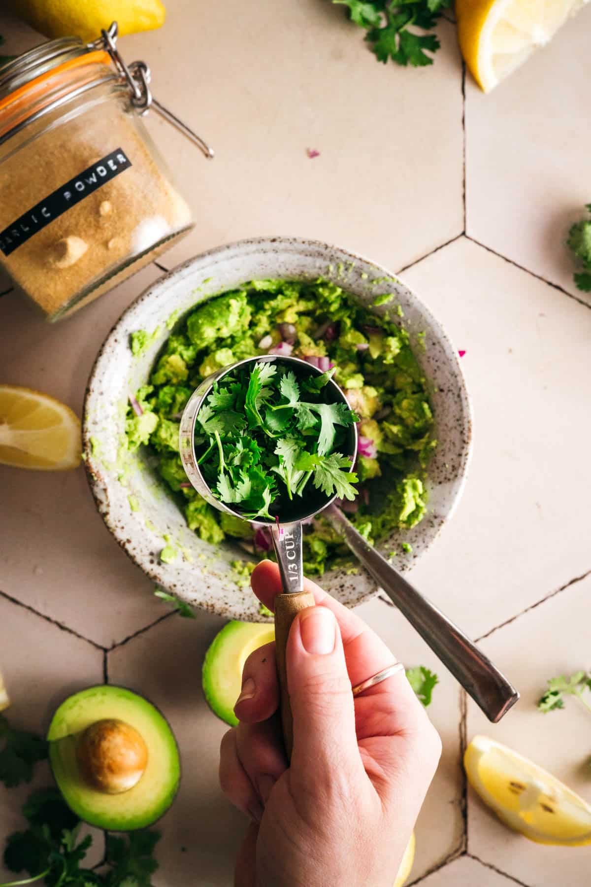 Cilantro being added to a bowl of mashed avocado.