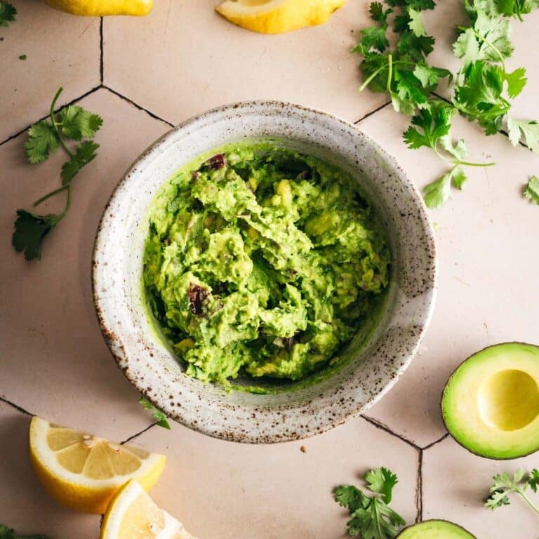 Fresh homemade guacamole with avocado, lemon and herbs on a tile counter.