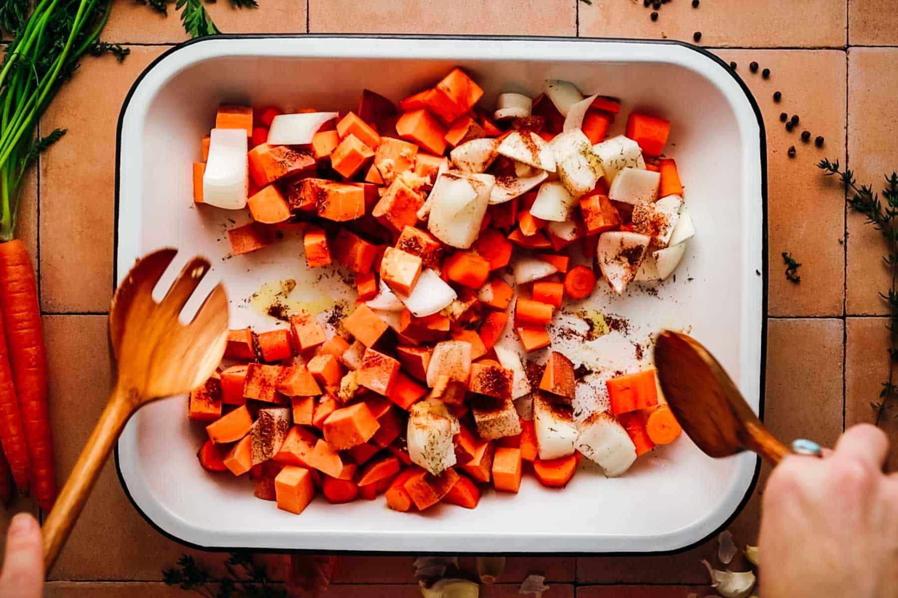 Woman mixing chopped carrots, sweet potatoes, and seasonings together.