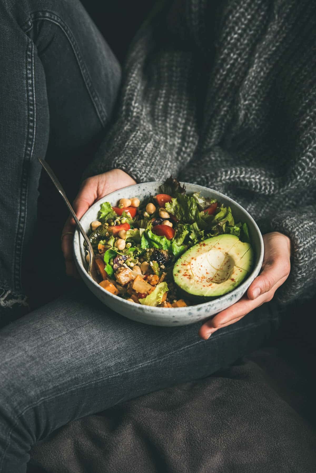 Bowl of a whole foods plant based meal in a large bowl being held by a woman wearing black.