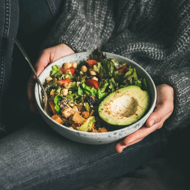 Bowl of a whole foods plant based meal in a large bowl being held by a woman wearing black.