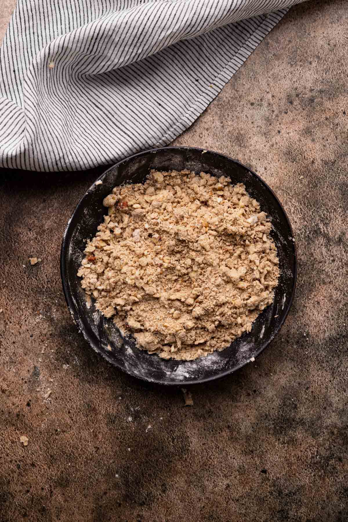 Combining streusal topping ingredients in a shallow black ceramic bowl.