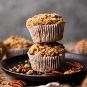Banana pecan muffins with a streusel top with white wrappers on a small black plate.