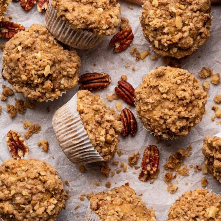 Fresh muffins on a rectangle piece of parchment paper with pecans around.