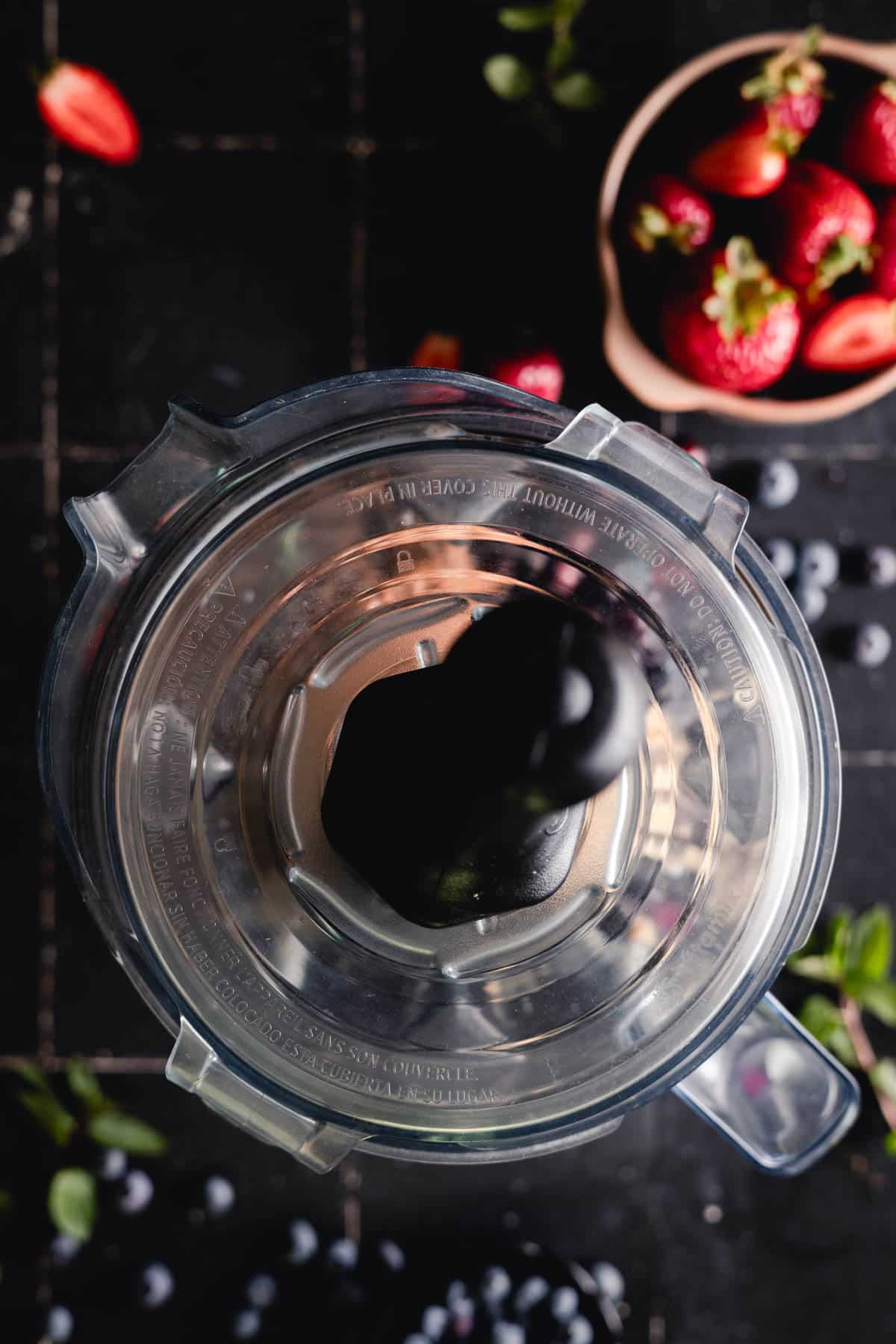 Blender lid and tamper placed on top of Vitamix blender pitcher.