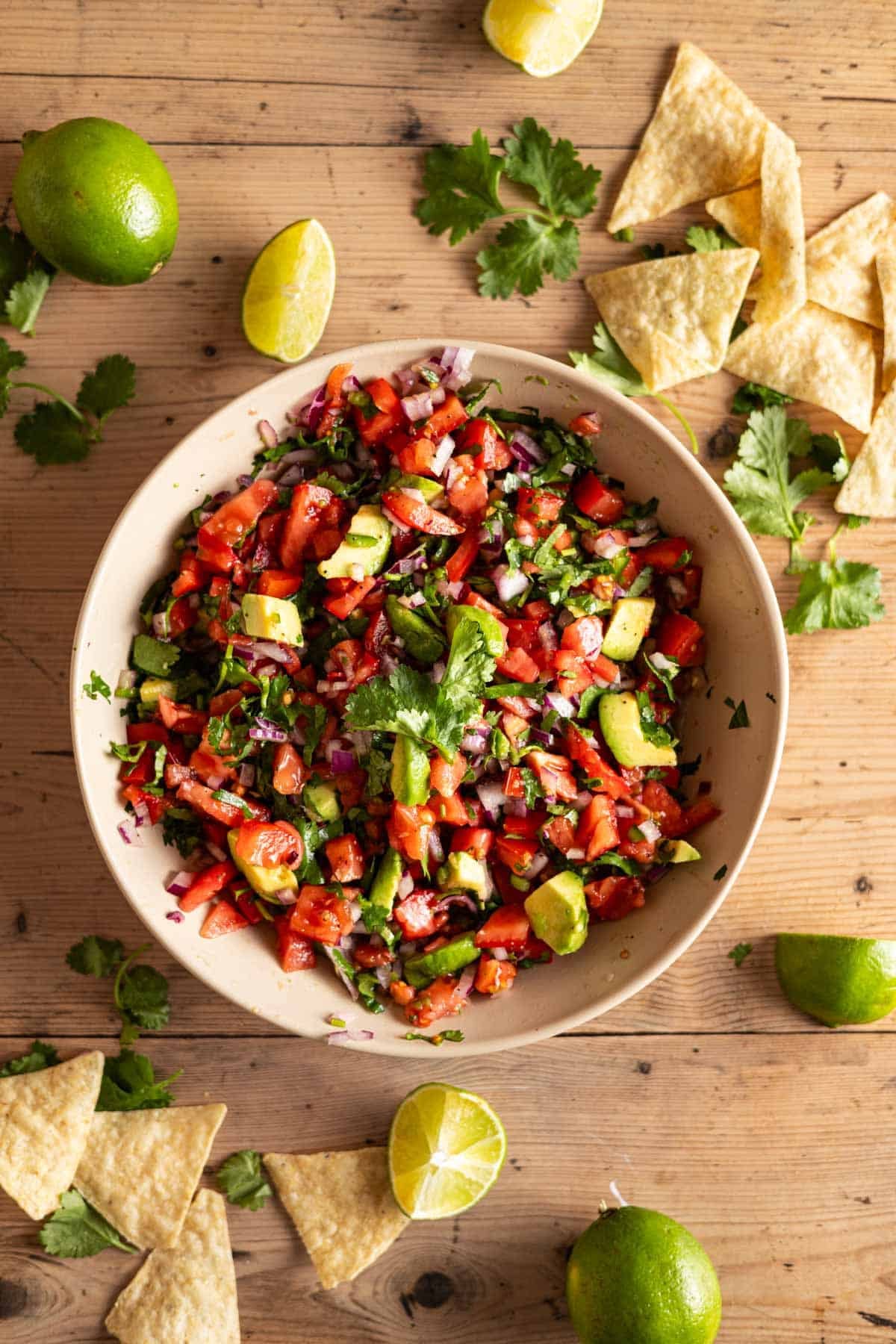 Homemade avocado pico in a shallow cream bowl with lime wedges and cilantro sprigs next to it.