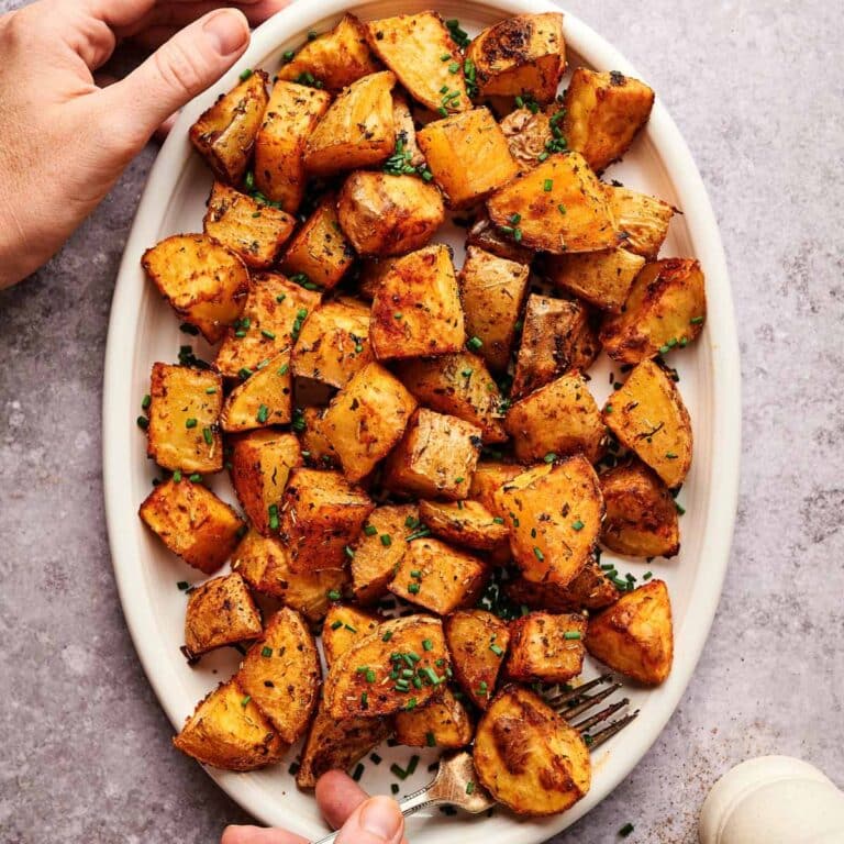 Hands reaching for oval plate of baked home fries.