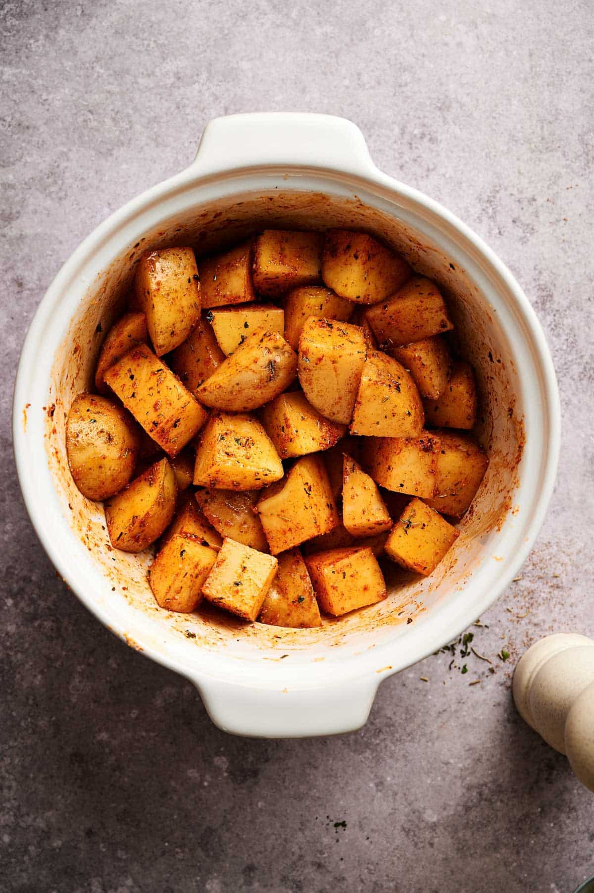 All of the ingredients for baked home fries in a white dish mixed together.
