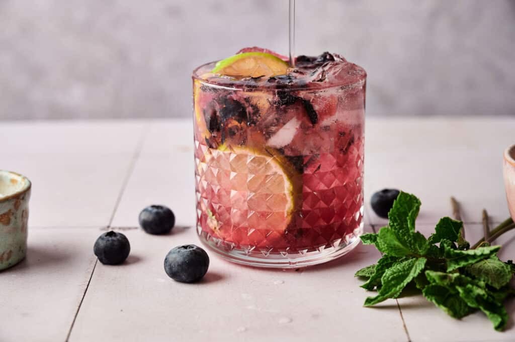 Blueberry mocktail in a clear glass cup with fresh blueberries and int on the side.