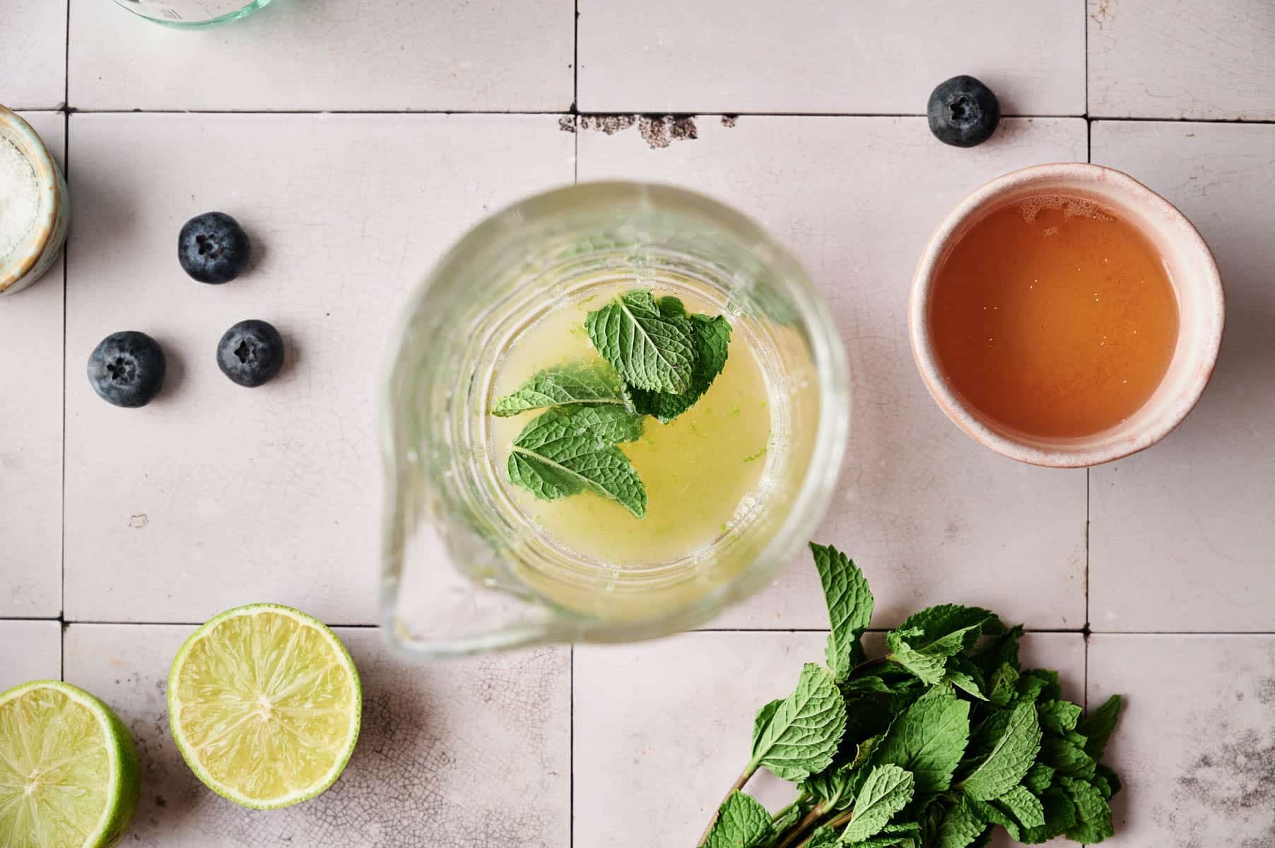 Adding ingredients into a small glass pitcher to make blueberry mocktail.