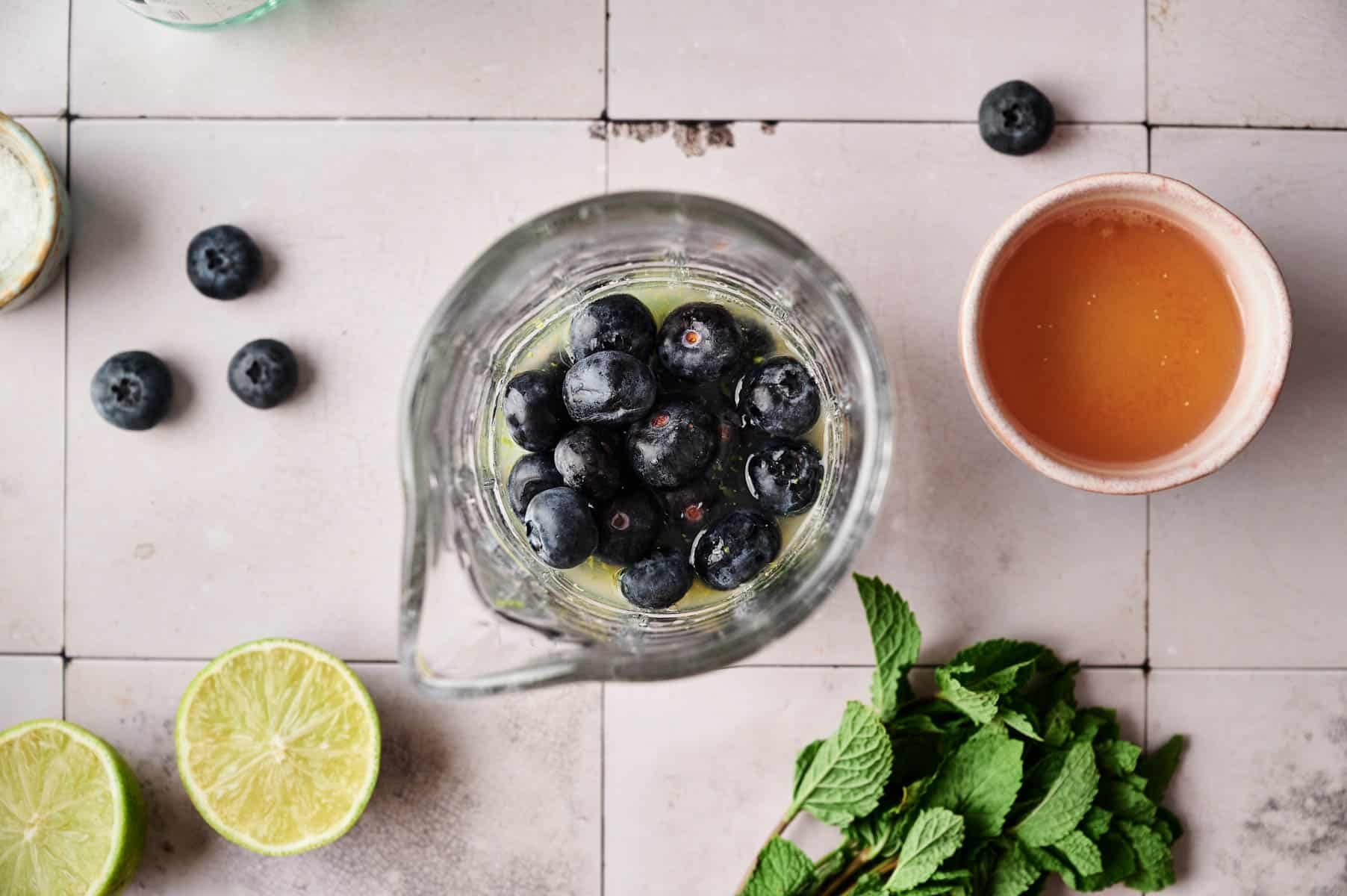 Adding ingredients into a small glass pitcher to make blueberry mocktail.