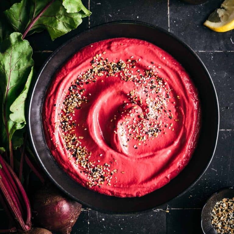 Fresh beet hummus in a large black bowl on a black tiled counter.