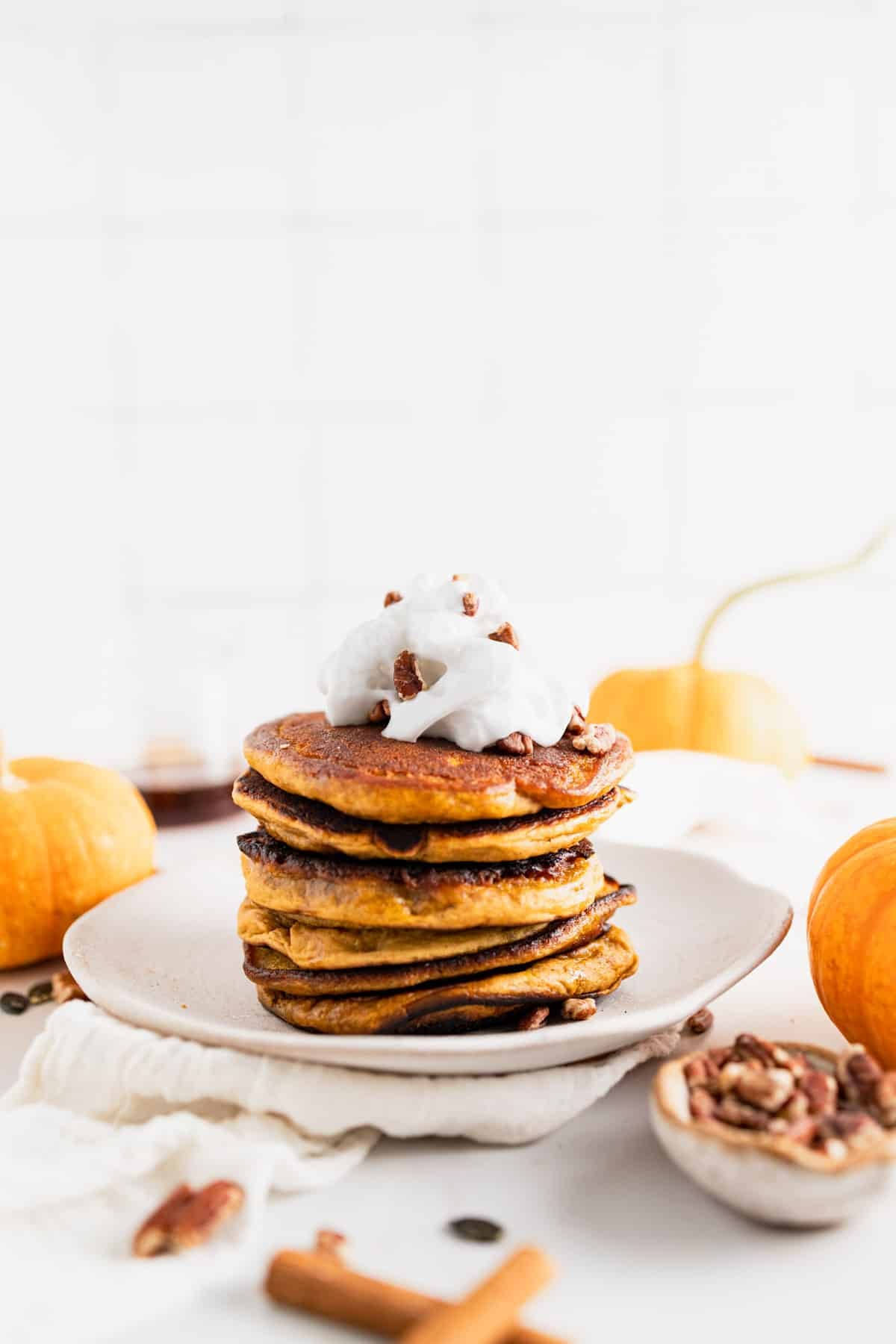 Tall stack of pumpkin spice pancakes with vegan whipped cream on top.