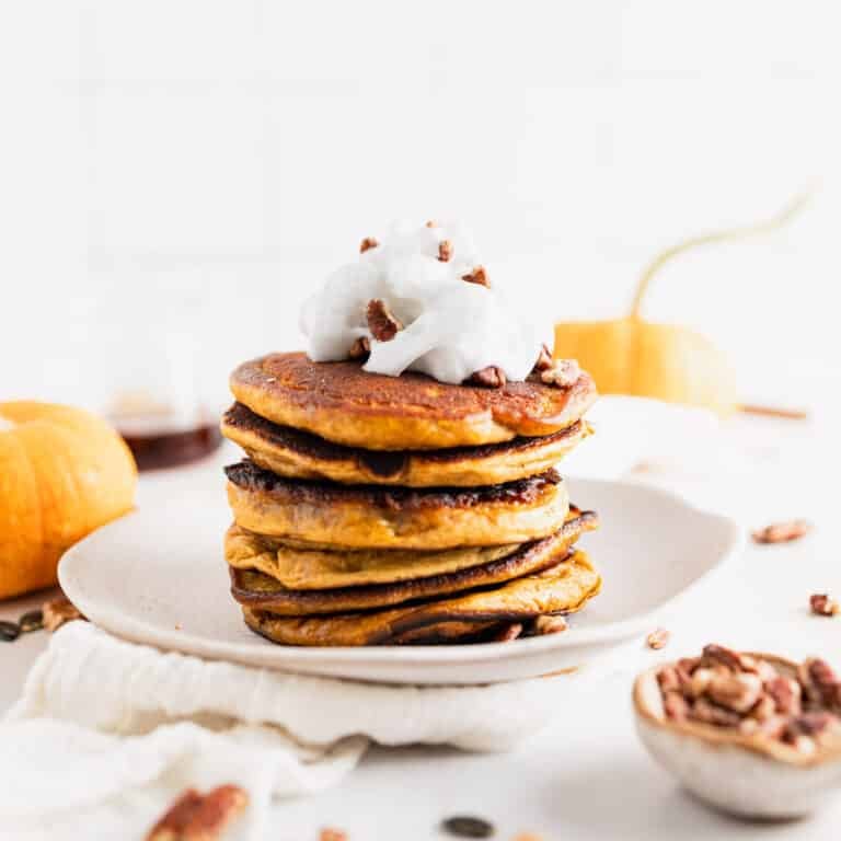 Tall stack of pumpkin spice pancakes with vegan whipped cream on top.