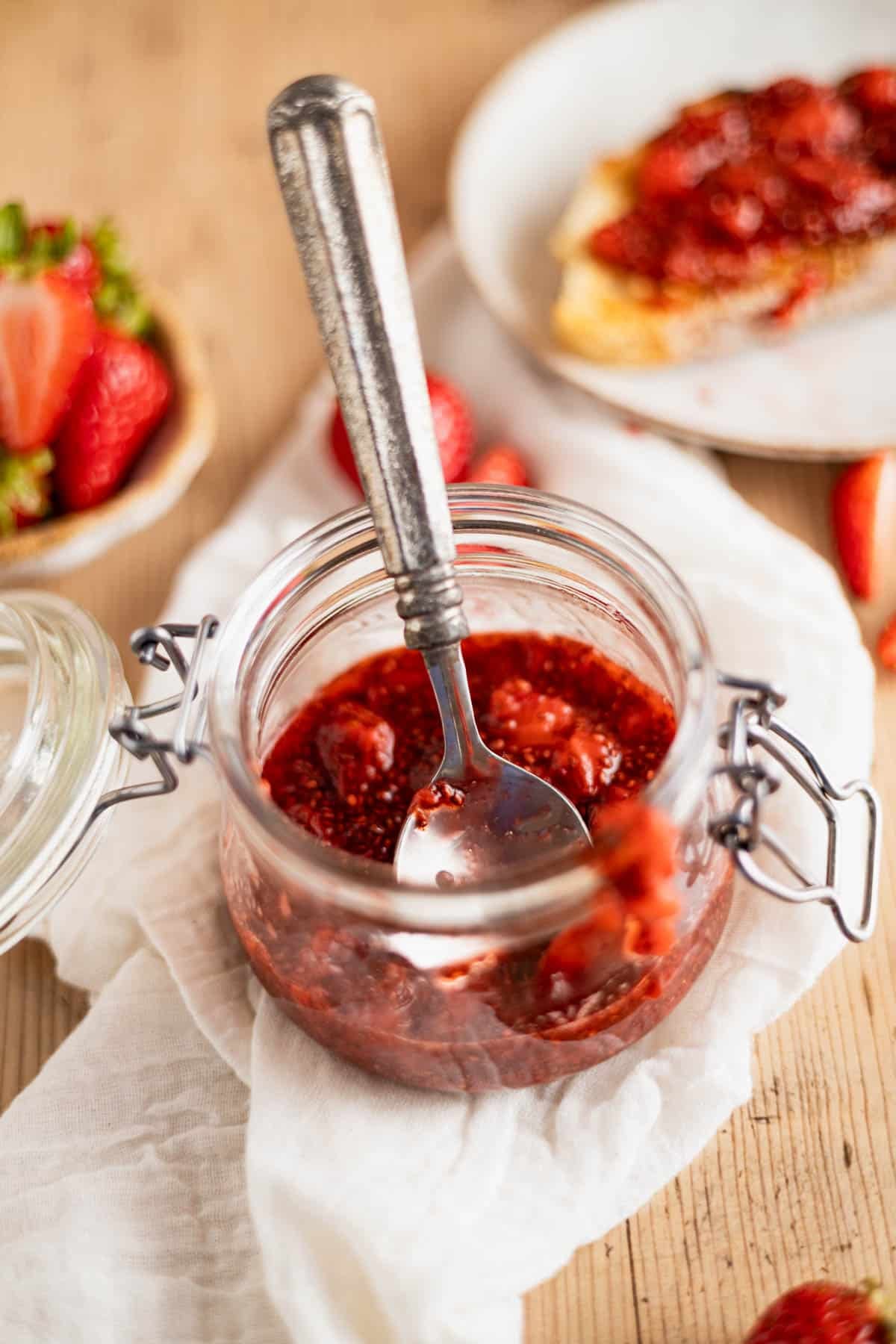 Chia seed strawberry jam in a glass jar on a white linen napkin.