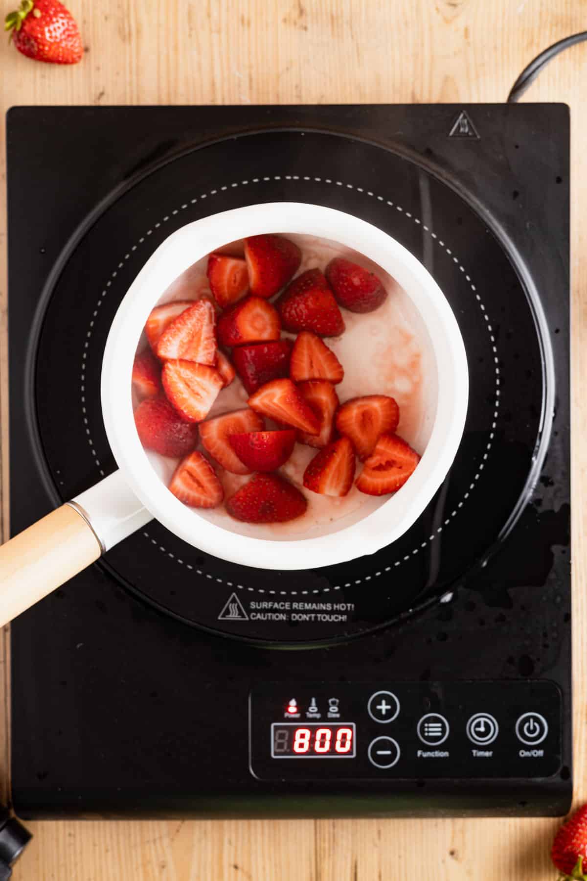 Adding fresh strawberries to a pot on a cook top.