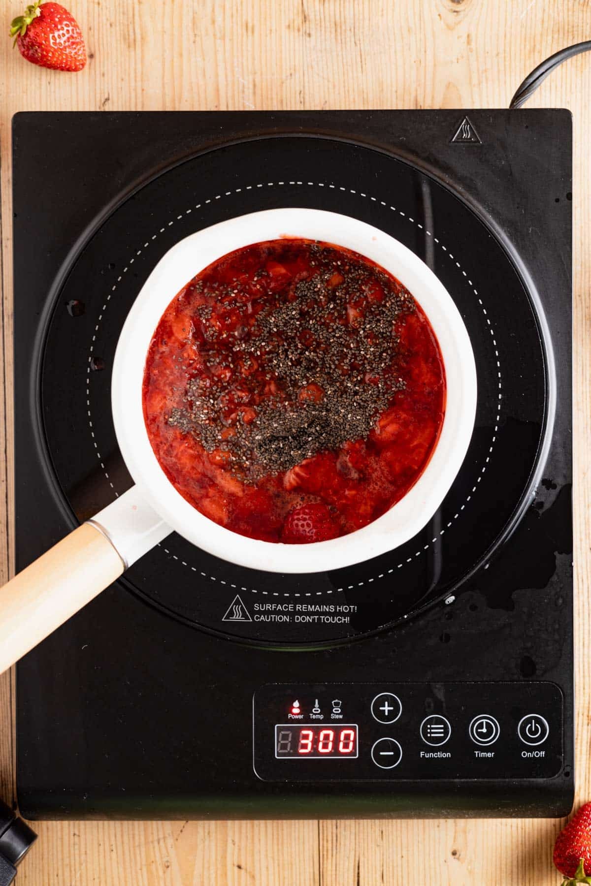 All the ingredients for chia seed strawberry jam in a white saucepan with a wooden handle.