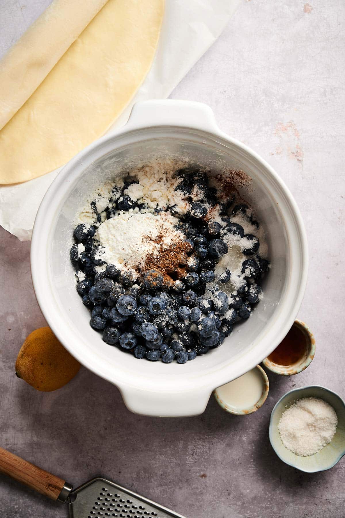 Combining filling ingredients in a large mixing bowl for blueberry pie.