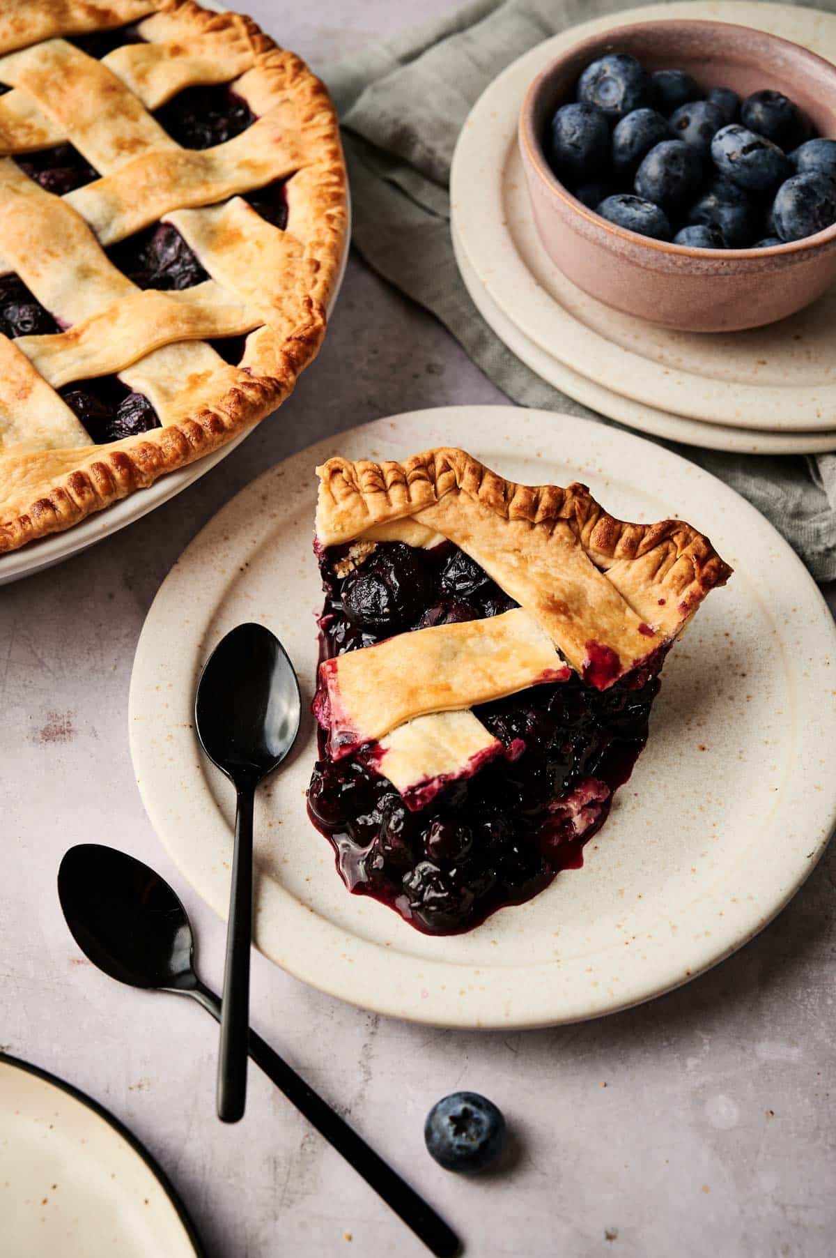 A slice of berry pie on a white plate with black spoons next to it.