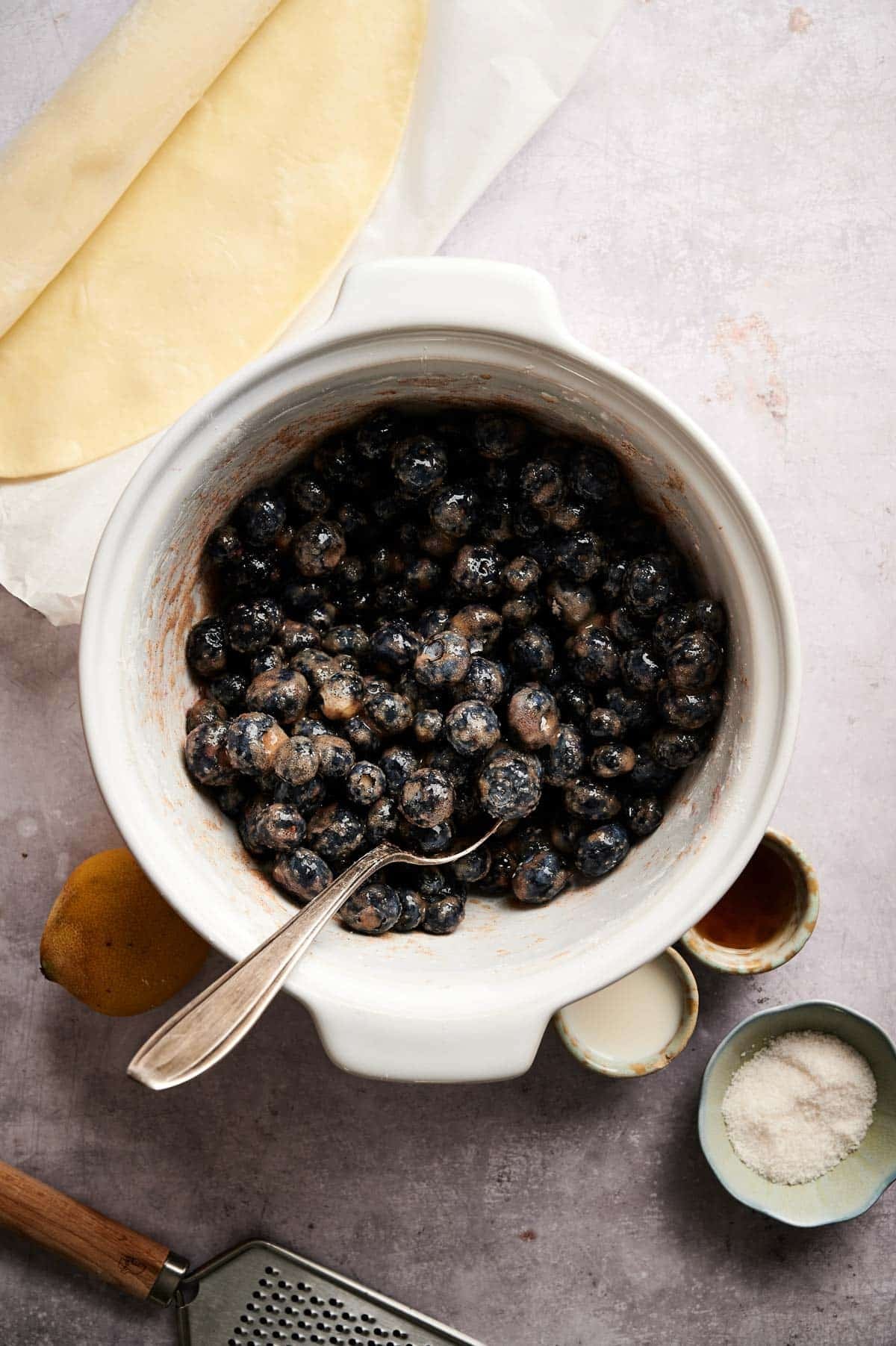 Combining filling ingredients in a large mixing bowl for blueberry pie.