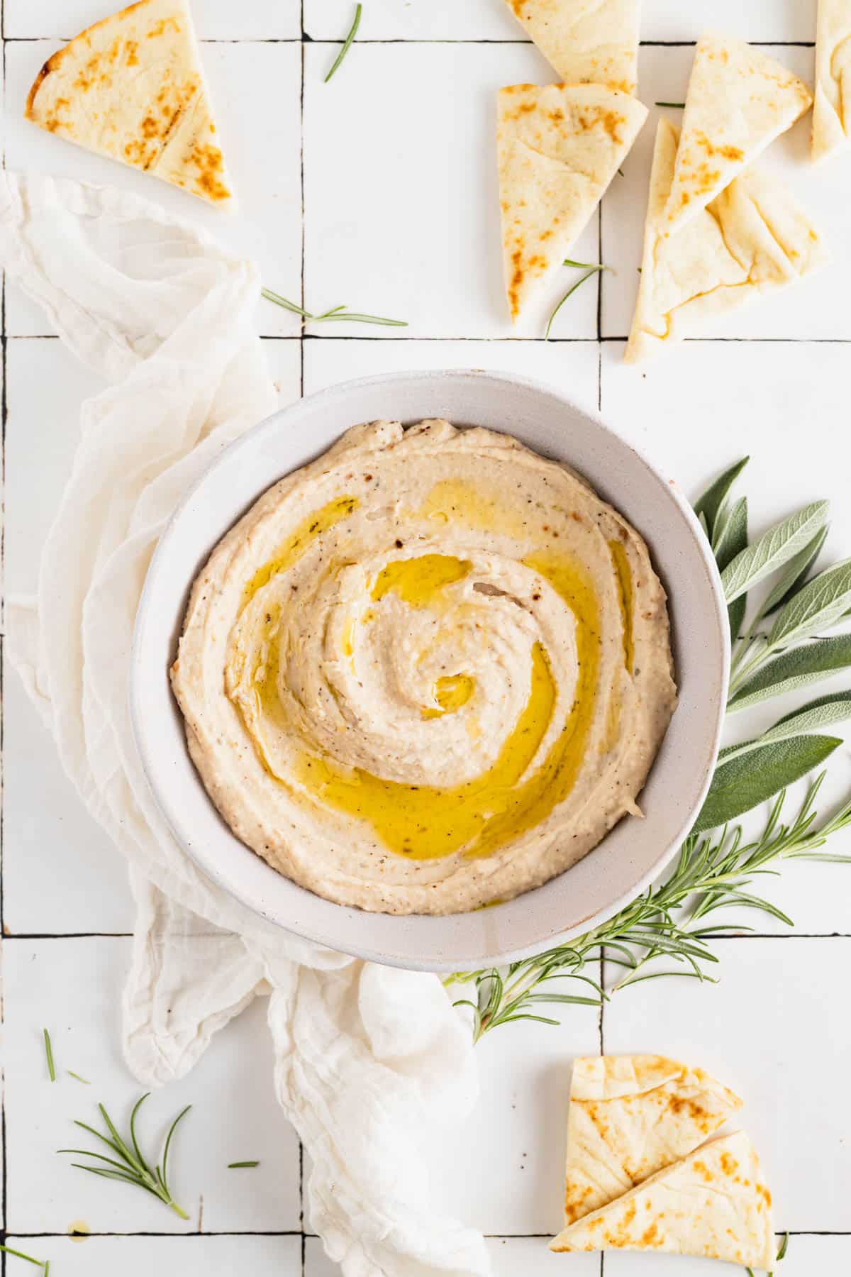 Homemade white bean dip in a white bowl with olive oil drizzled on top.