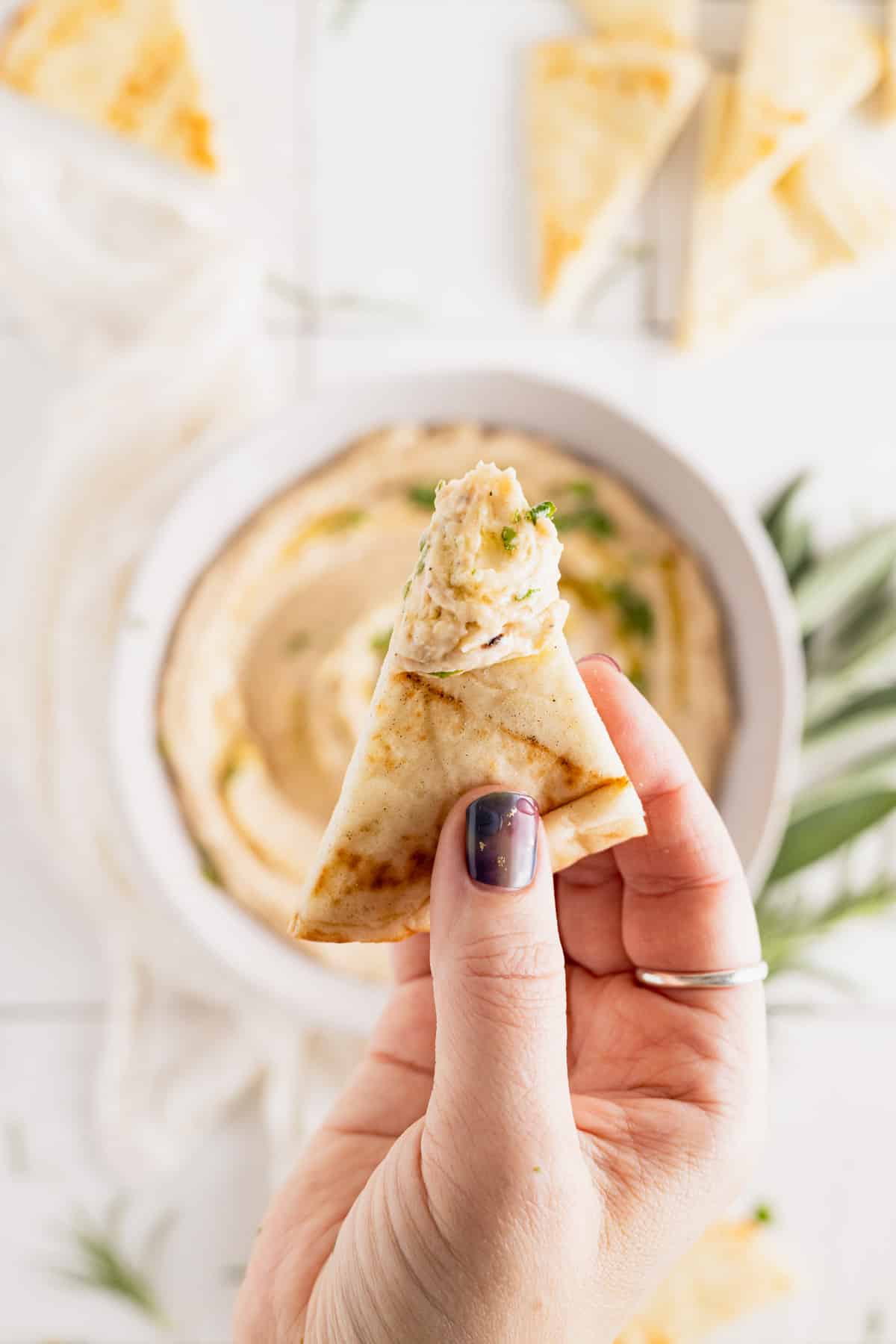 Italian bean dip on a slice of pita bread in a womans hand.