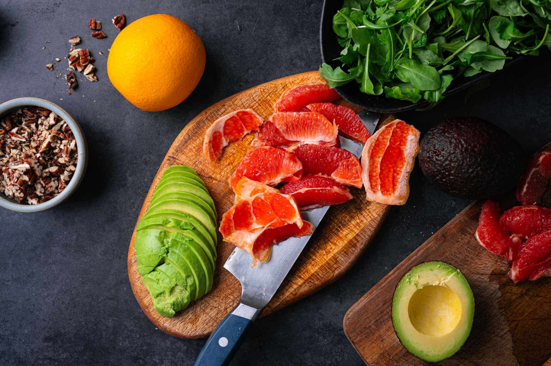 Oranges and avocado sliced on a wooden cutting board.