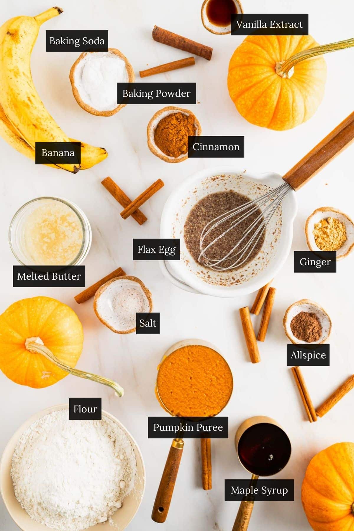 Ingredients for homemade banana pumpkin muffins with each ingredient labeled on a white marble counter.