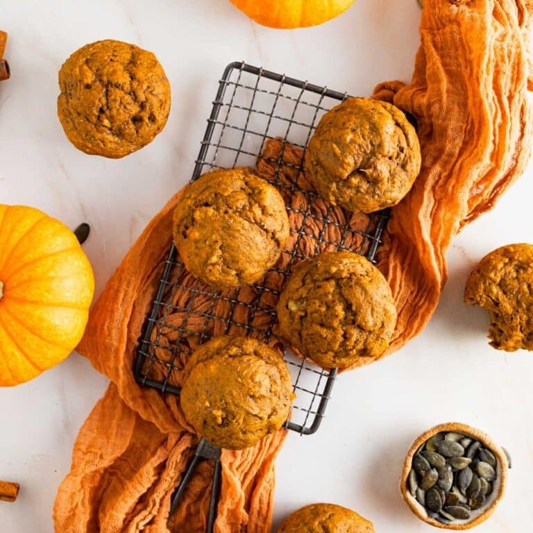 Fluffy banana pumpkin muffins on a small cooking rack with an orange gauze napkin underneath.