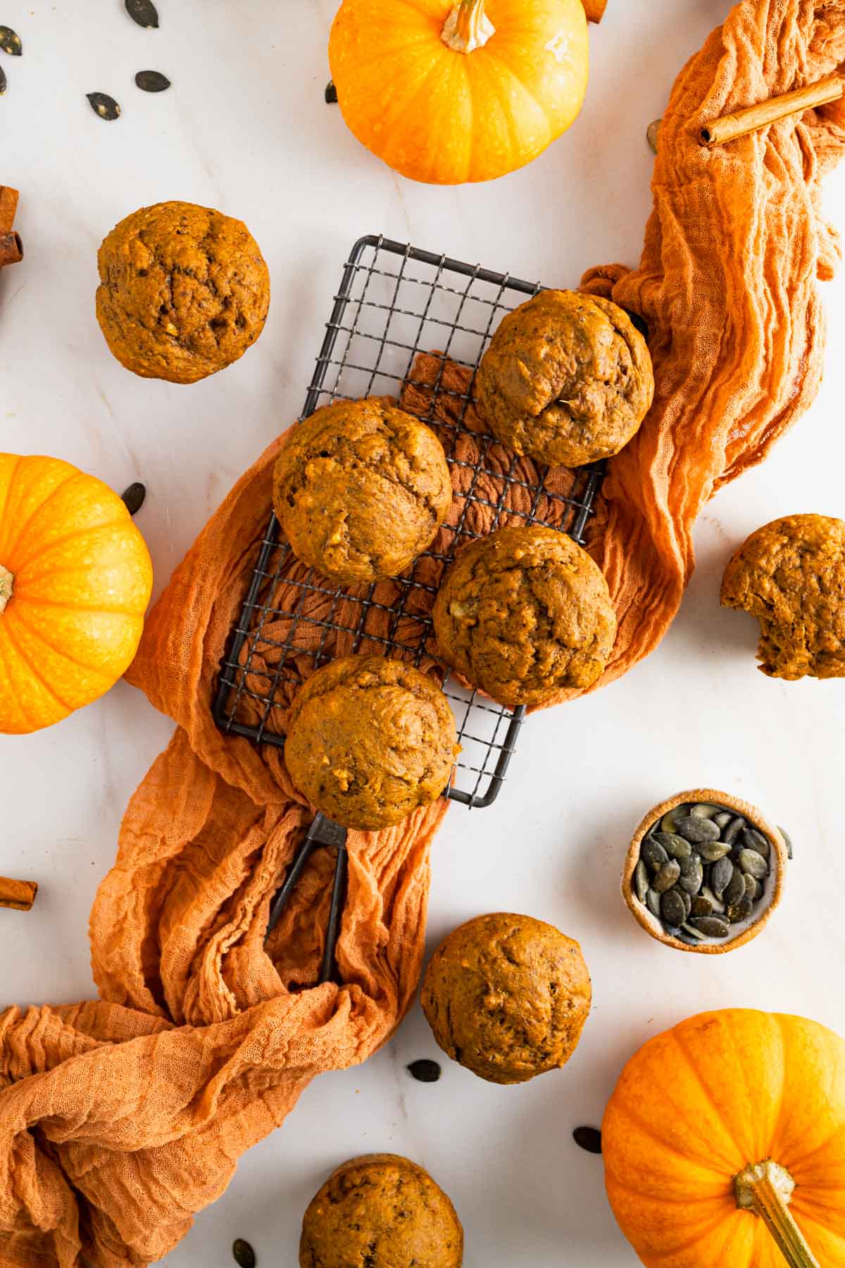 Fluffy banana pumpkin muffins on a small cooking rack with an orange gauze napkin underneath.