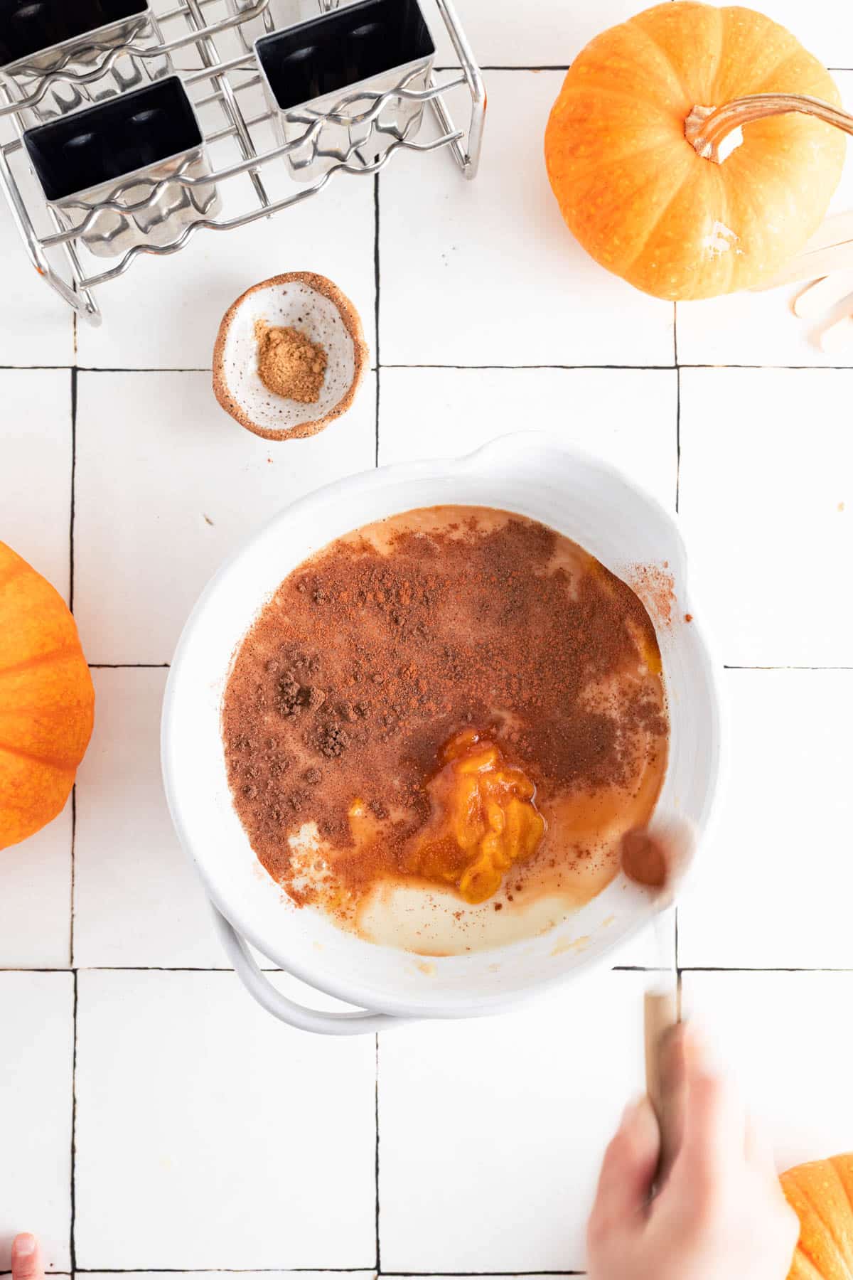 Adding all the ingredients for pumpkin popsicles to a mixing bowl.