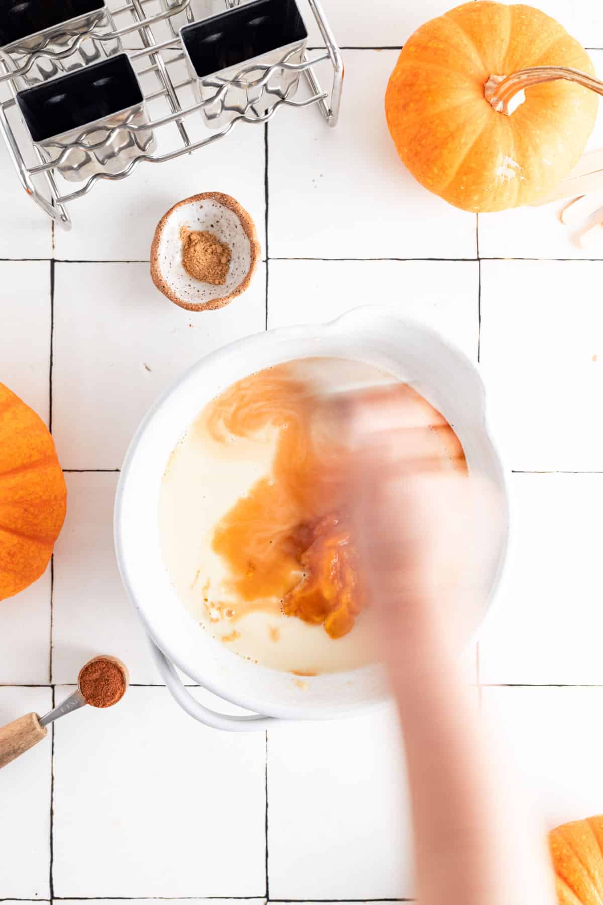 Adding all the ingredients for pumpkin popsicles to a mixing bowl.