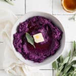 Vegan mashed sweet potatoes on white tile counter with fresh sage and butter.