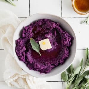 Vegan mashed sweet potatoes on white tile counter with fresh sage and butter.